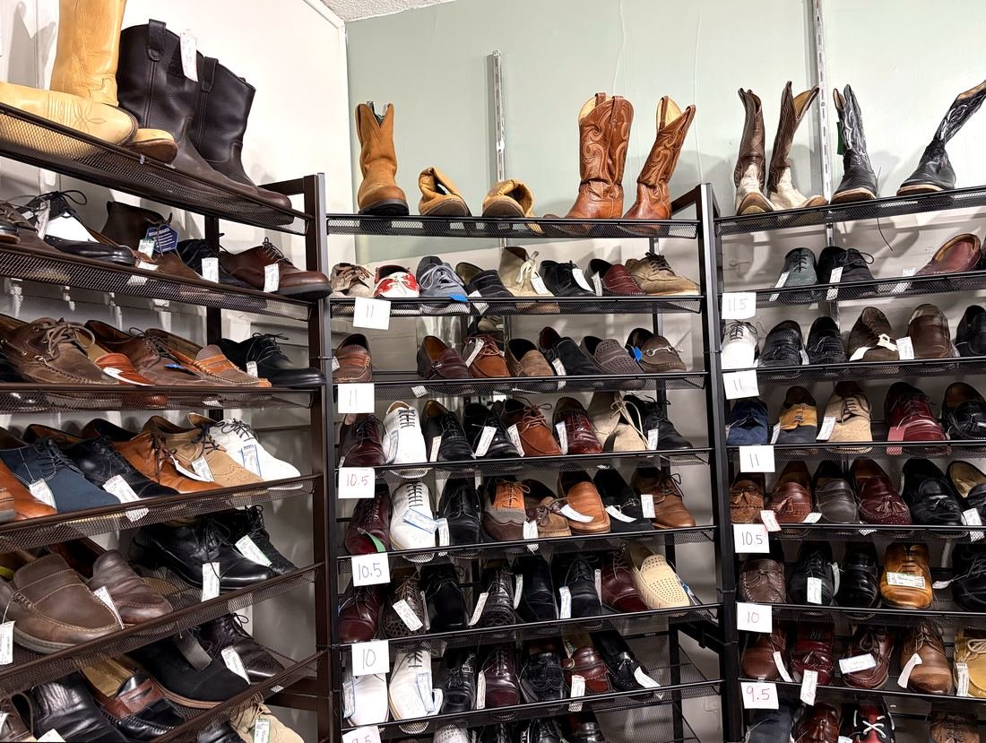 Metal shelves of men's dress shoes sorted by size — oxfords, loafers, wingtips and monk straps — with cowboy boots along the top.